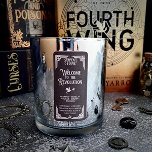 May include: A silver candle jar with a black label that reads "Serpent & Flame" and "Welcome to the Revolution". The candle is officially licensed and made with paraffin soy wax. The candle is 11.5 oz (326g).
