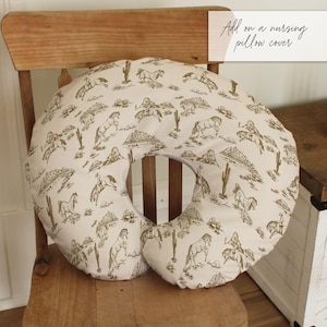 Puede incluir: Una funda de almohada de lactancia con fondo crema y un estampado marr&oacute;n de tem&aacute;tica occidental. El estampado incluye caballos, jinetes, cactus e ilustraciones de monta&ntilde;as. La almohada es circular con una almohada m&aacute;s peque&ntilde;a adjunta.