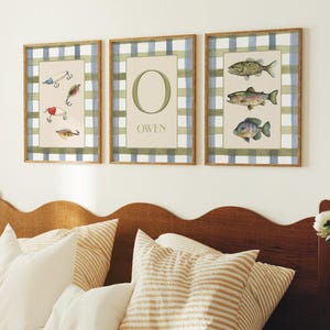 May include: Three framed wall art pieces. One features fishing lures, another displays the letter "O" and the name "OWEN", and the third showcases three fish. Each has a plaid border in blue, green, and white.