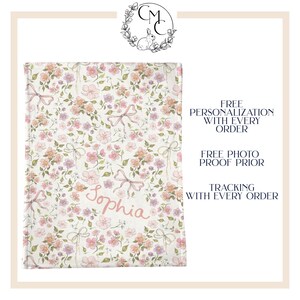 Puede incluir: Una manta de beb&eacute; blanca con un patr&oacute;n floral rosa y el nombre "Sophia" escrito en rosa.