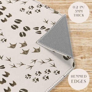 May include: A white area rug with a brown animal footprint pattern. The rug has a 0.2 inch / 5 mm thick backing and hemmed edges.