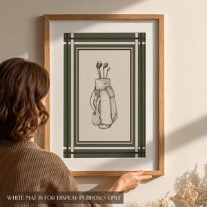 May include: A framed print featuring a detailed sketch of a golf bag with clubs. The artwork is set against a cream background, framed by a green and brown border, and encased in a light brown wooden frame. The text at the bottom reads: WHITE MAT IS FOR DISPLAY PURPOSES ONLY.