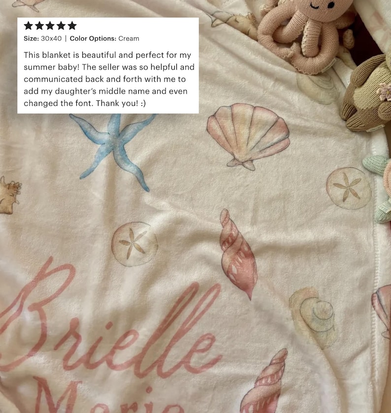 May include: Cream-colored baby blanket with watercolor seashell and starfish designs. The blanket measures 30x40 inches and features the name "Brielle" in pink script. The blanket is decorated with various sea-themed illustrations.