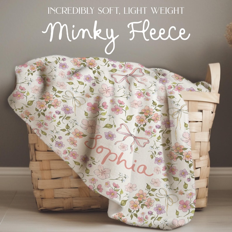 Puede incluir: Una manta de microfibra minky suave y ligera con un patr&oacute;n floral en tonos de rosa, morado y verde. La manta tiene un nombre personalizado, "Sophia", en una fuente de letra rosa.