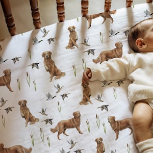 Peut inclure: Drap de lit de bébé blanc avec un motif répété de golden retrievers, de canards et de roseaux. Les chiens sont représentés dans diverses poses, et les canards sont en vol. Le drap est en tissu doux et respirant.