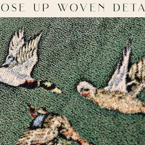 May include: Close-up of a tapestry with a green background and three white birds woven into the fabric. The birds are flying in different directions and have detailed features.