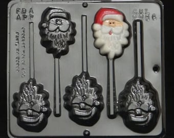 Puede incluir: Un molde de plástico gris para hacer piruletas de caramelo. El molde tiene cinco cavidades, cuatro de las cuales tienen forma de cara de Papá Noel y una tiene forma de muñeco de nieve. El molde tiene un soporte para palos para cada cavidad.