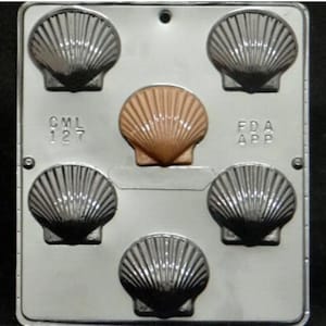 May include: A white plastic mold with six scallop shell shapes. The mold has the text "CML 127" and "FDA APP" on it.