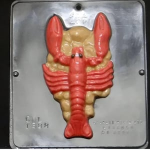 May include: A red plastic mold for making candy shaped like a lobster. The mold has a detailed design of the lobster's body and claws. The mold is made of plastic and has a shiny finish. The mold is labeled "CUL 1288" and "AMERICAN MADE 1288 61 2024".