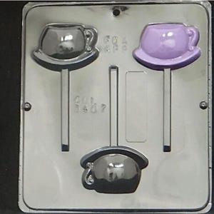 Könnte beinhalten: Eine Plastikform zum Herstellen von Schokoladen-Lollies. Die Form hat drei Vertiefungen, die jeweils die Form einer Teetasse mit Henkel haben. Die Teetassen sind in verschiedenen Farben: schwarz, lila und schwarz. Die Form hat einen Stielhalter für jede Vertiefung.