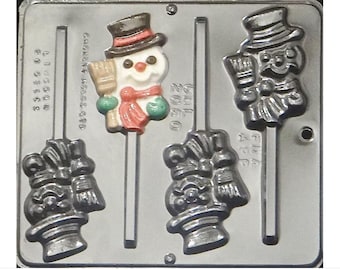 Puede incluir: Un molde de metal para hacer piruletas de muñeco de nieve. El molde tiene tres cavidades, cada una con un diseño de muñeco de nieve. El muñeco de nieve lleva un sombrero de copa negro, una bufanda roja y una escoba en una mano. El molde está hecho de metal y tiene un acabado plateado.