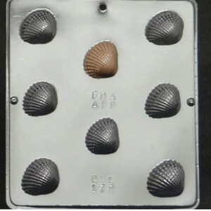 May include: A silver metal mould with eight shell-shaped cavities. The mould has the text "FDA APP" and "C.I. 172" on it.
