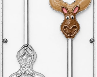 May include: A clear plastic candy mold featuring two cavities for moose-shaped lollipops. One cavity is empty, while the other contains a detailed, painted moose head with brown fur, pink inner ears, and black eyes, all attached to a stick channel.