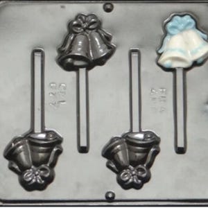 May include: A black plastic mold for making chocolate lollipops. The mold has four cavities, each shaped like a pair of wedding bells. Two cavities have a blue ribbon and two cavities have a white ribbon.