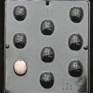 Puede incluir: Un molde de plástico gris con ocho cavidades con forma de cerebro. El molde está diseñado para hacer chocolate o caramelos. El molde tiene el texto "FDA 495" en la parte delantera.