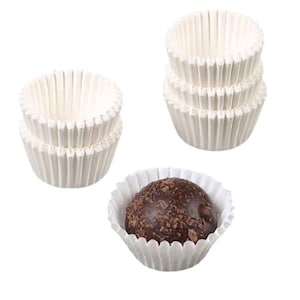 May include: White paper cupcake liners, also known as baking cups, are stacked in a pile. A single chocolate truffle sits inside a white paper liner.