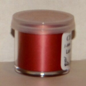 May include: A small clear jar with a red metallic powder inside. The jar has a white lid and a label that says "Copper Aluminum Lustre".