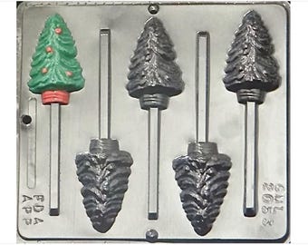 Puede incluir: Un molde de metal para hacer piruletas de chocolate con forma de árbol de Navidad. El molde tiene cinco cavidades, cuatro de las cuales tienen forma de árbol de Navidad con un diseño de corteza texturizado. La quinta cavidad tiene forma de árbol de Navidad con una superficie lisa verde y adornos rojos. Cada cavidad tiene un agujero para insertar un palo de piruleta.