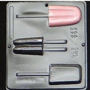 Może przedstawiać: Srebrna metalowa forma do robienia lodów na patyku. Forma ma trzy sekcje, jedną dla pojedynczego lodu na patyku i dwie dla podwójnych lodów na patyku. Forma jest oznaczona "FDA APP" i "2.5 OZ."