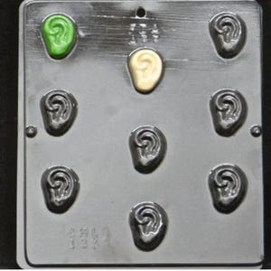 May include: A rectangular, silver-colored mold with nine ear-shaped cavities. Two cavities are filled with green and yellow-colored material, while the remaining cavities are empty. The mold has a small hole at the top and text at the bottom.