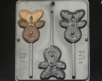 Puede incluir: Un molde plateado para hacer piruletas de chocolate con forma de reno y muñeco de nieve. El molde tiene dos diseños de reno y un diseño de muñeco de nieve. El molde está etiquetado como "FDA Approved" y "CHIL 2133".