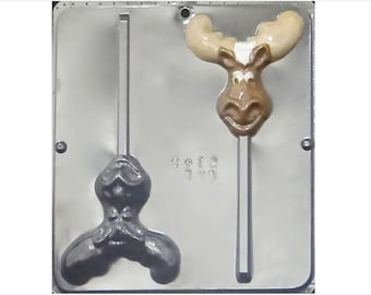 Puede incluir: Un molde de plástico para hacer piruletas de chocolate. El molde tiene dos cavidades, una con forma de cabeza de alce y la otra con forma de persona con pajarita. El molde es plateado y tiene el número "512" impreso en él.