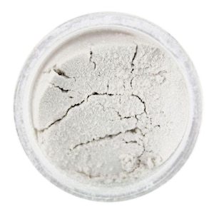 May include: A small, round container filled with white powder. The powder is slightly textured and has a few cracks in it.