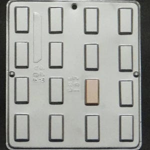 Op de afbeelding: Een zilveren metalen mal met 12 rechthoekige holtes voor het maken van chocolade repen. De mal heeft een verhoogde rand rond elke holte en een glad oppervlak.