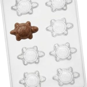 May include: A clear plastic rectangular candy mold tray featuring eight identical turtle-shaped cavities. One brown chocolate turtle is resting inside the second cavity on the left side, while the other seven cavities remain empty and transparent.