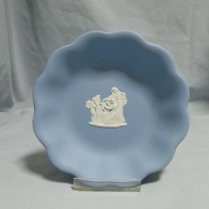May include: A light blue ceramic trinket dish with a white raised design of a woman and two children. The dish has a scalloped edge.