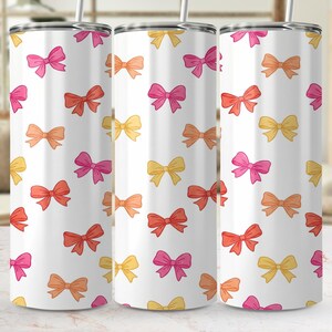 Könnte beinhalten: Drei weiße Isolierbecher mit einem sich wiederholenden Muster aus bunten Schleifen in Rosa-, Orange- und Gelbtönen. Jeder Becher hat einen silbernen Strohhalm. Die Schleifen sind gleichmäßig über die Oberfläche der Becher verteilt.