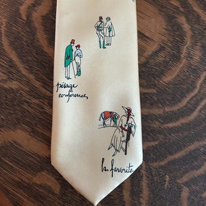 May include: Cream-colored silk tie with equestrian-themed illustrations in red, green, and black. The tie features drawings of horse racing scenes and figures, with French text accents. The words "le defilé", "pesage conference", and "la favorite" are written on the tie.