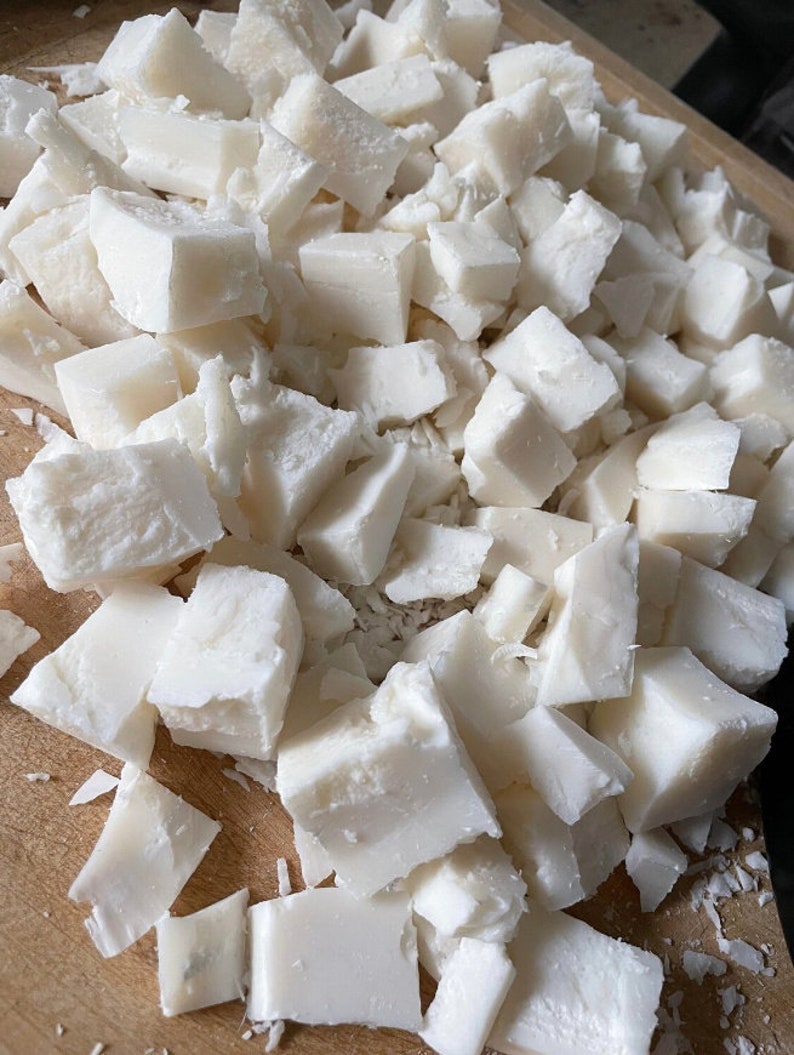 May include: A close-up of a wooden cutting board covered in small, white, cubed pieces of coconut.