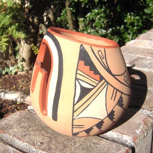 May include: A hand-painted ceramic pot with a geometric design in shades of brown, white, and black. The pot has a unique shape with a cutout on one side.