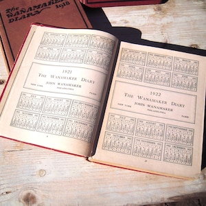 May include: An open vintage diary with calendars for the years 1921 and 1922. The diary is titled "The Wanamaker Diary" and features the name "John Wanamaker" with the locations "New York", "Philadelphia", and "Paris".