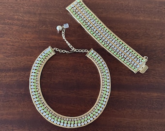 May include: A gold necklace and bracelet set with alternating clear and light green rhinestones. The jewelry is on a brown wooden surface.
