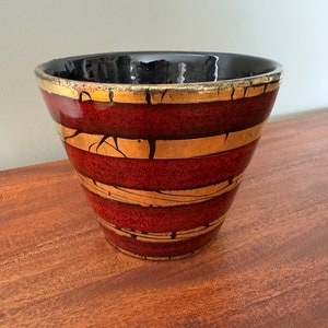May include: A red ceramic planter with gold stripes. The planter has a black glaze on the inside and a distressed look.
