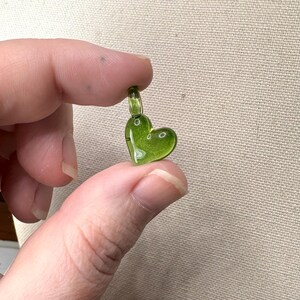 May include: A small, green glass heart charm with a loop at the top for attaching to a necklace or bracelet.