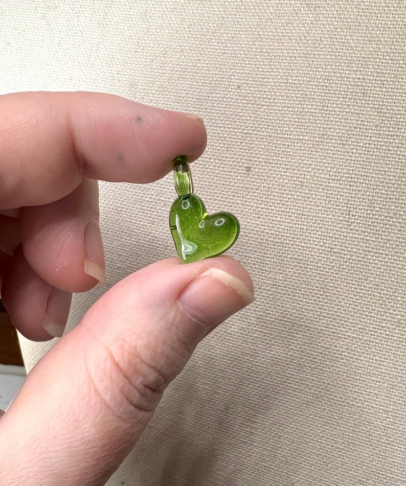 May include: A small, green glass heart charm with a loop at the top for attaching to a necklace or bracelet.