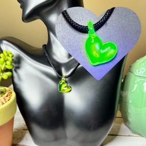 May include: A black cord necklace with a bright green glass heart pendant. The heart pendant glows under a black light.