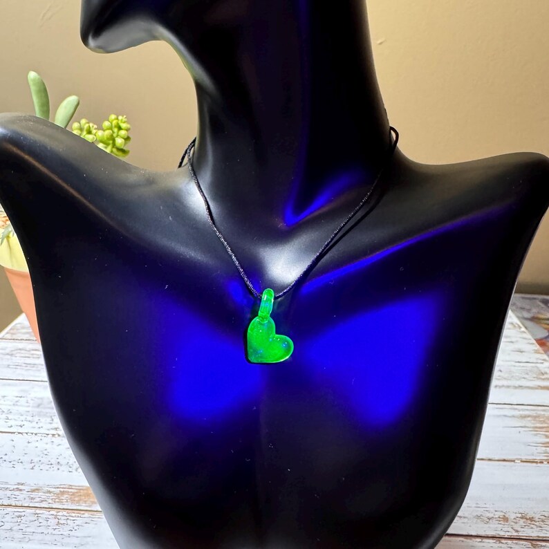 May include: A green heart-shaped pendant necklace on a black cord. The pendant is made of resin and has a glittery finish.