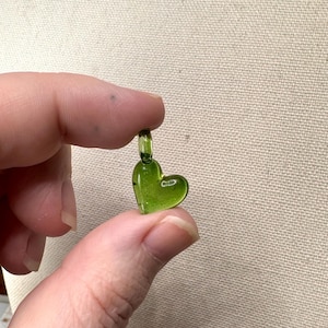 May include: A small, green glass heart charm with a loop at the top for hanging.