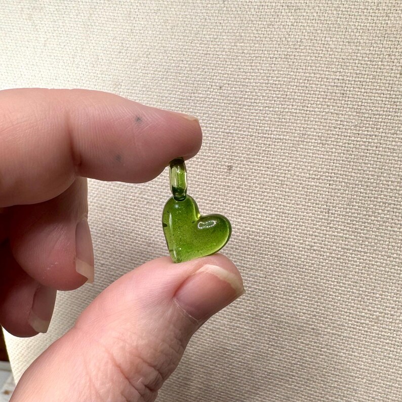 May include: A small, green glass heart charm with a loop at the top for hanging.