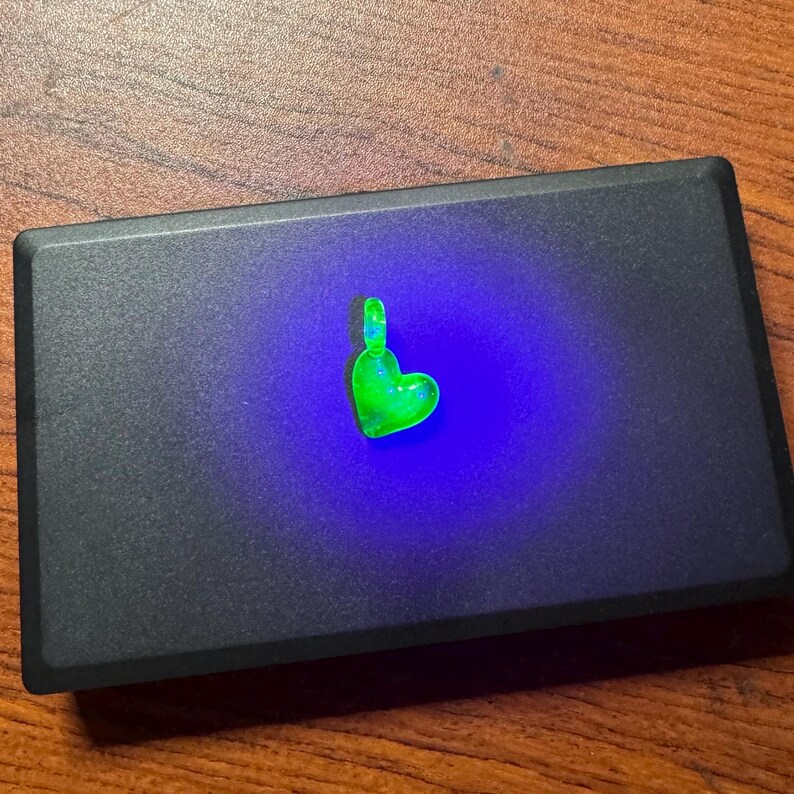May include: A small green heart-shaped pendant with a shiny, sparkly finish. The pendant is illuminated with a bright blue light.