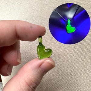 May include: A small green glass heart pendant with a silver loop for hanging. The pendant glows green under a black light.