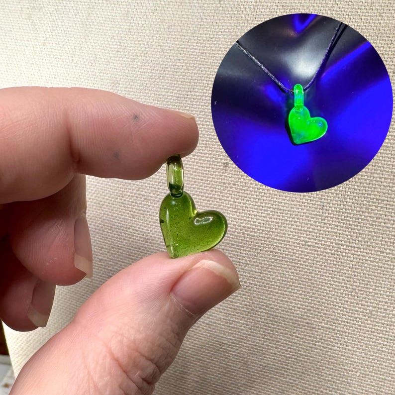 May include: A small green glass heart pendant with a silver loop for hanging. The pendant glows green under a black light.