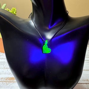 May include: A green glass heart pendant necklace on a black cord. The heart is glowing under a black light.
