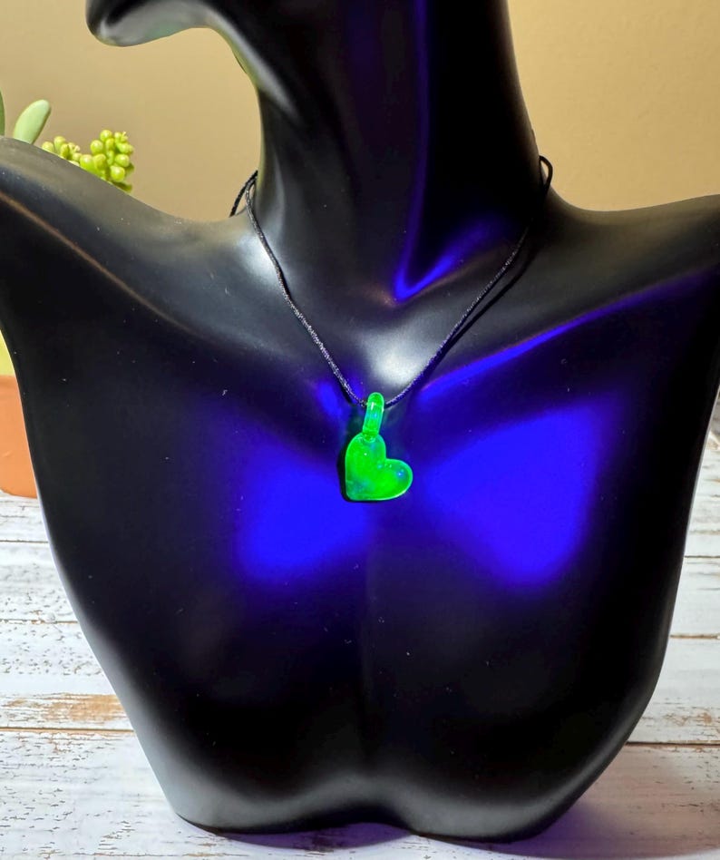 May include: A green glass heart pendant necklace on a black cord. The heart is glowing under a black light.