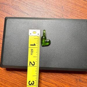 May include: A small, green glass heart charm with a loop at the top. The charm is about 1 inch in length.