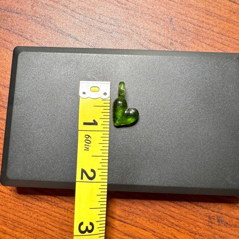 May include: A small, green glass heart charm with a loop at the top. The charm is about 1 inch in length.